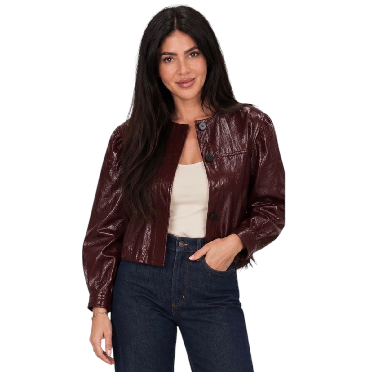 A woman modeling a cropped, glossy dark burgundy faux leather jacket over a cream tank top and dark blue jeans, set against a plain white background.