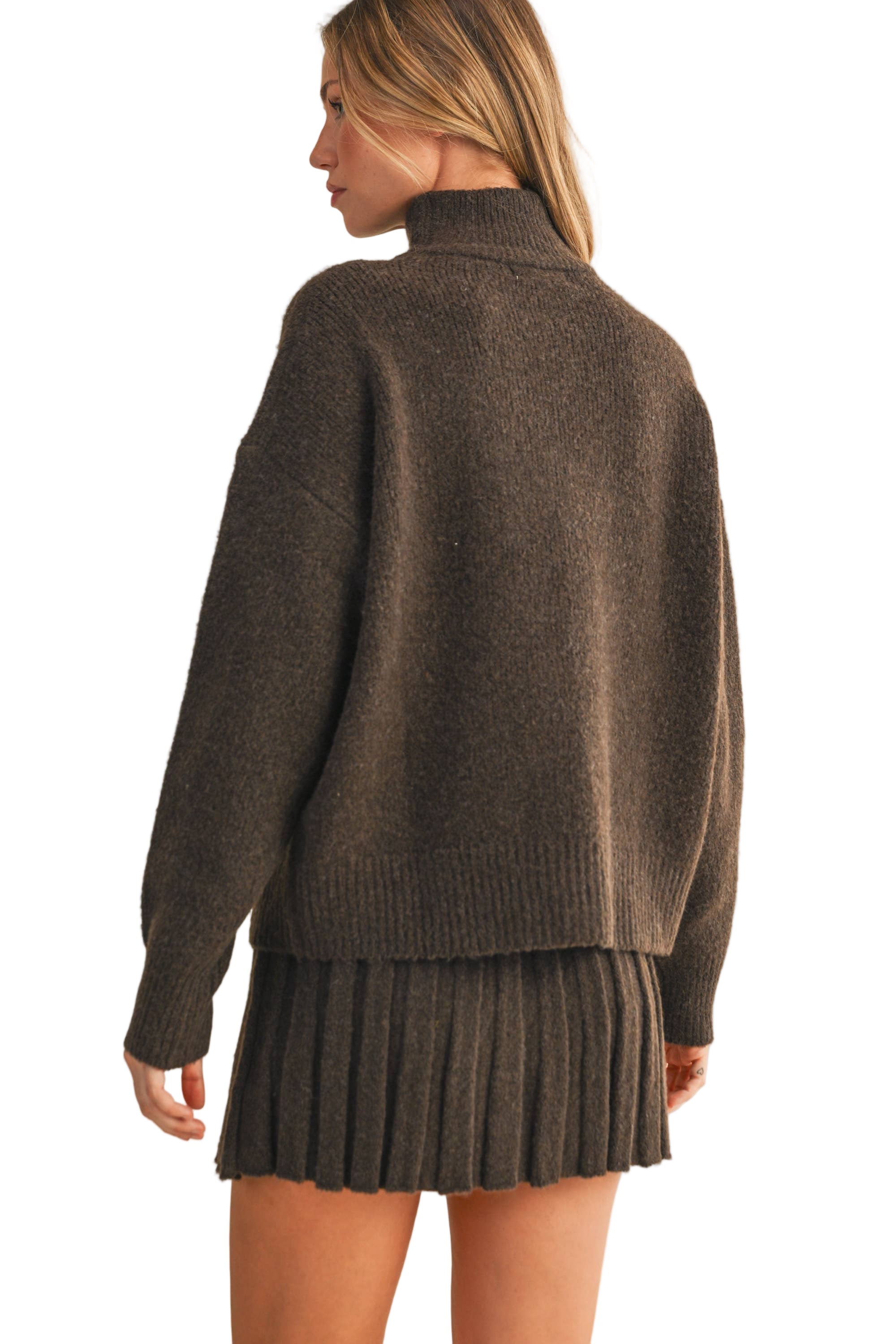 Woman wearing a brown sweater and pleated skirt on a beige background