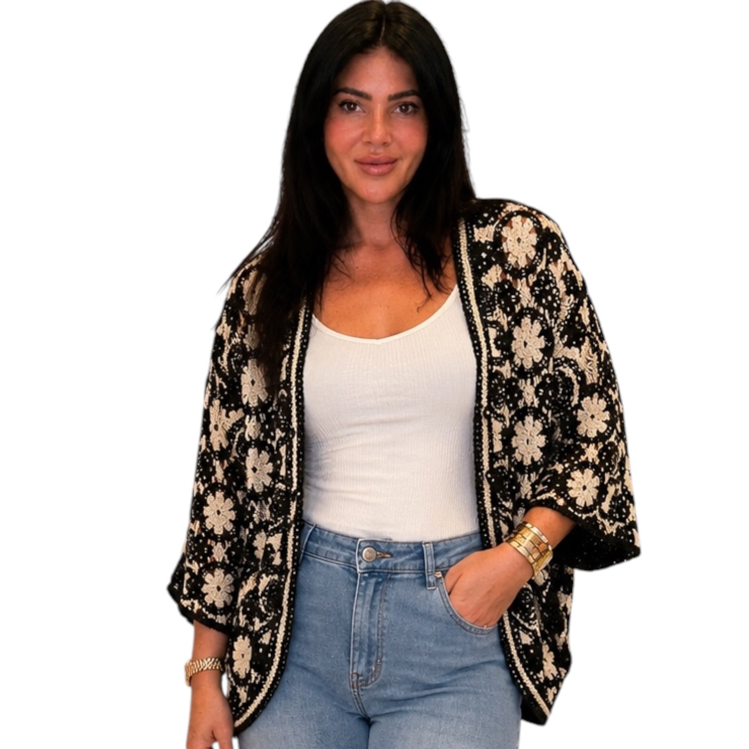Woman wearing a floral black and beige cardigan over a white top and blue jeans on a white background