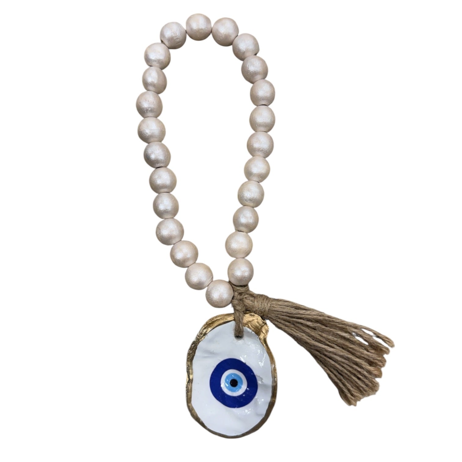A beaded necklace with round off-white pearls, a brown jute tassel, and a white oval charm featuring a blue and black evil eye design with a gold-toned border.