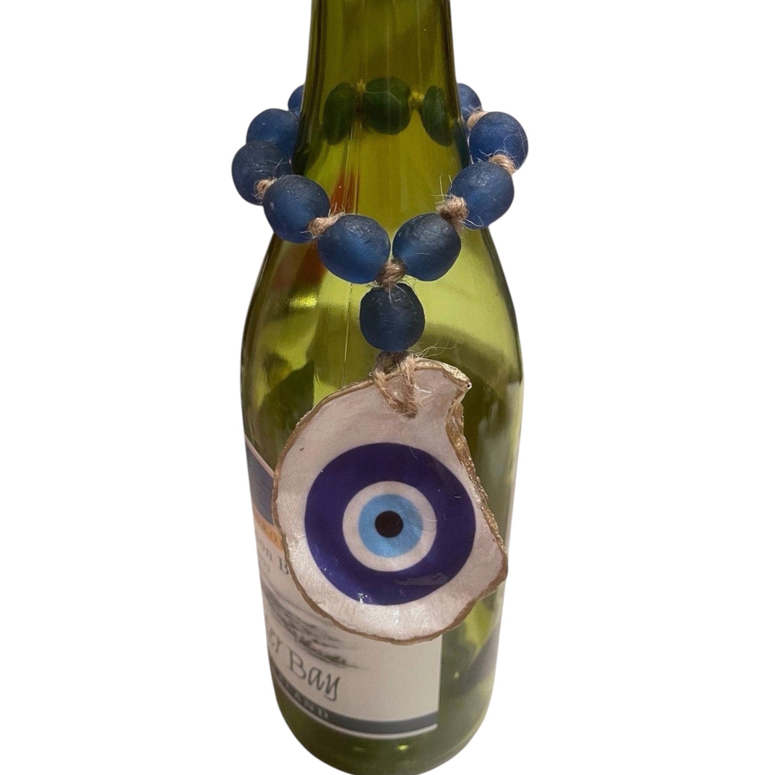 A green glass bottle decorated with a blue beaded bracelet and a large evil eye glass charm, shown against a plain white background.