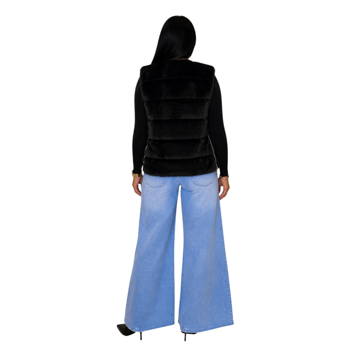 A woman shown from the back wearing a black faux-fur vest over a black long-sleeve top and light blue wide-leg jeans, against a plain white background.