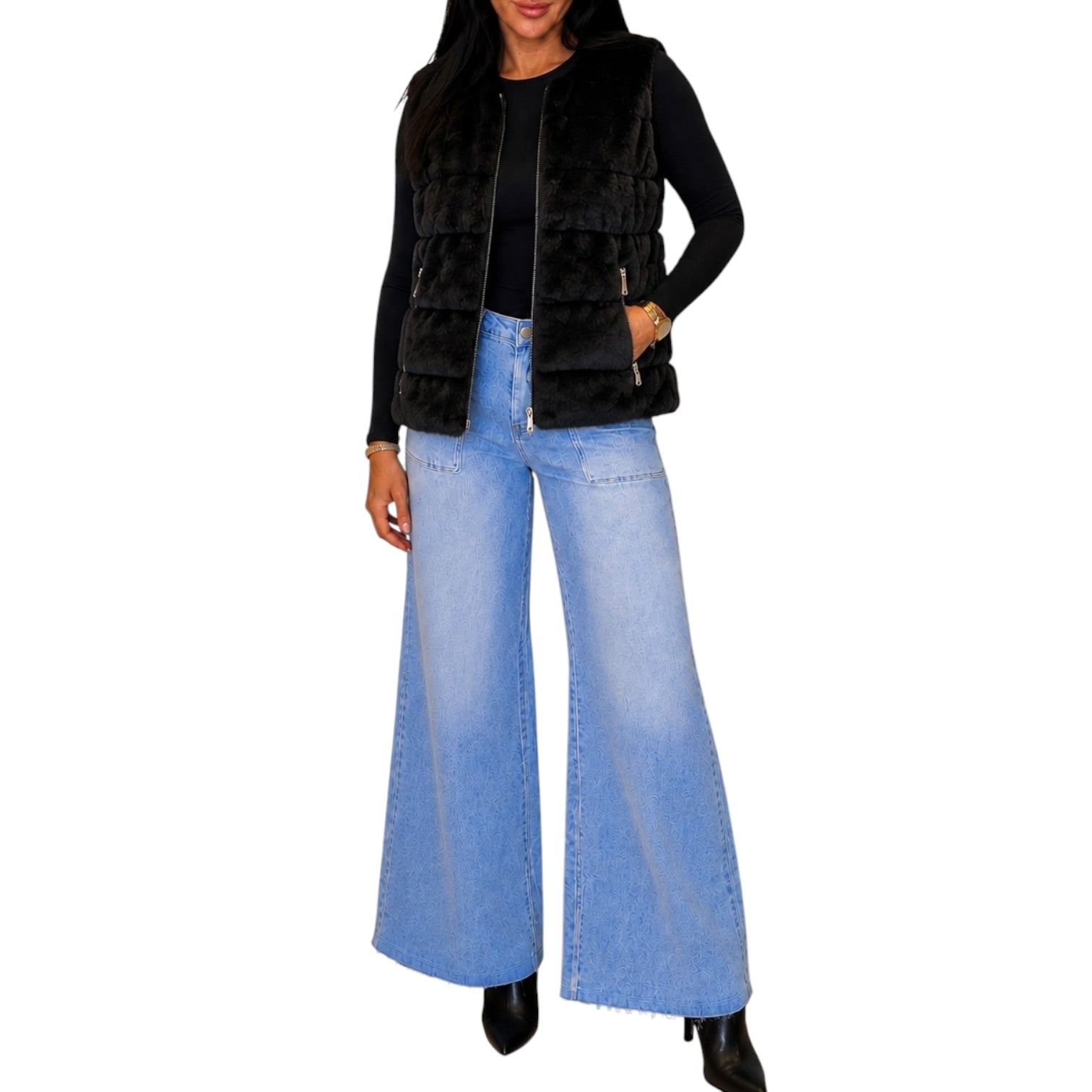 A woman wearing a black faux fur vest over a black long-sleeve top and light blue wide-leg denim jeans, shown against a plain white background.
