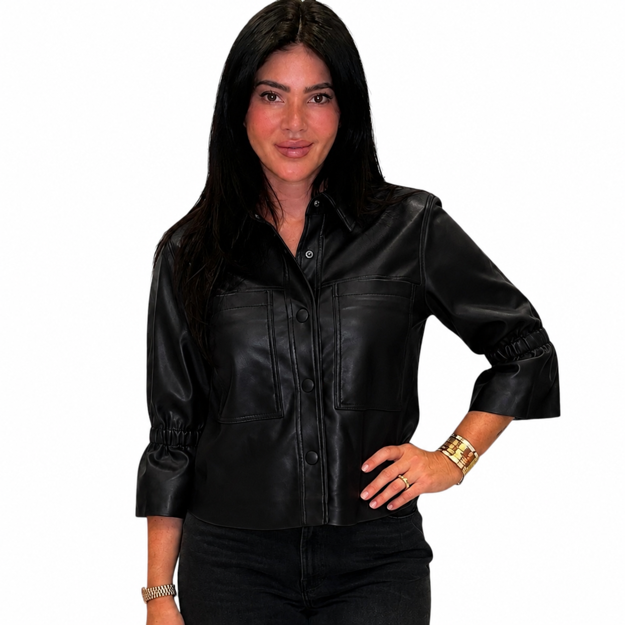 A woman modeling a black faux-leather button-up shirt jacket with three-quarter sleeves and chest pockets, set against a plain white background.