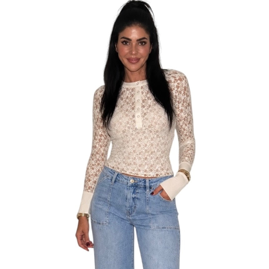 A woman modeling a beige and white floral lace long-sleeve crop top with a buttoned henley neckline, paired with light blue jeans, against a plain white background.