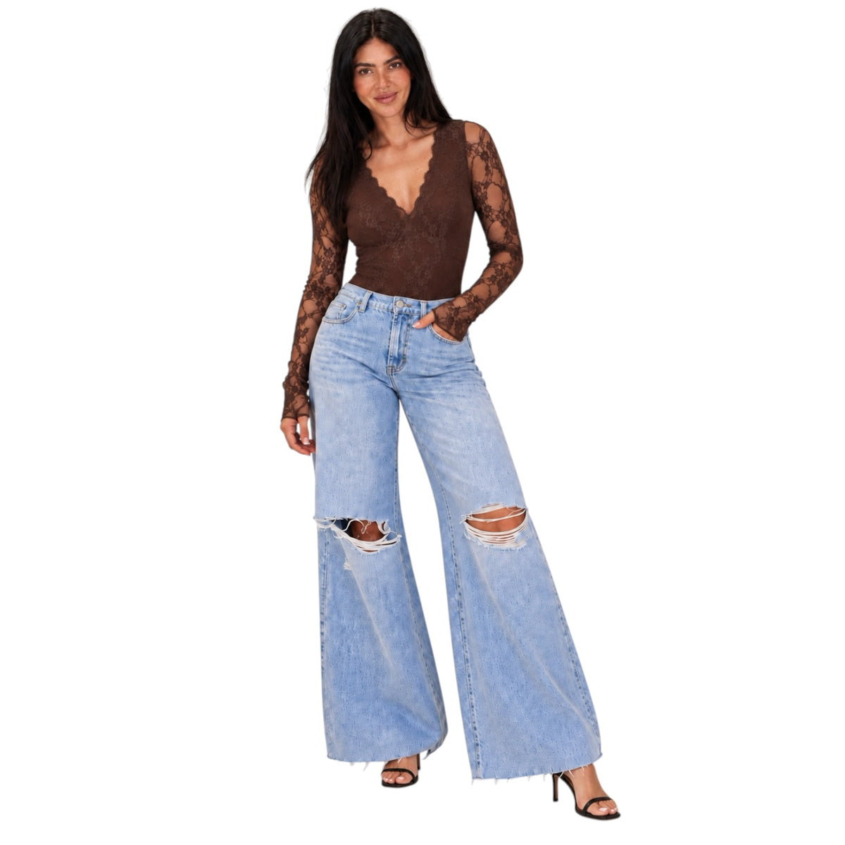 A woman modeling light-wash wide-leg distressed jeans with a brown lace long-sleeve top, standing against a plain white background.