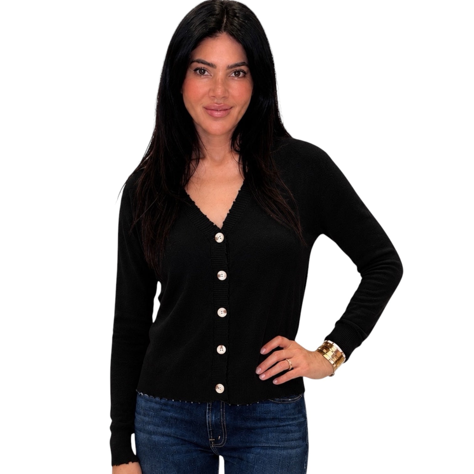 A woman modeling a black long-sleeve V-neck cardigan with white buttons, paired with blue jeans, against a plain white background.