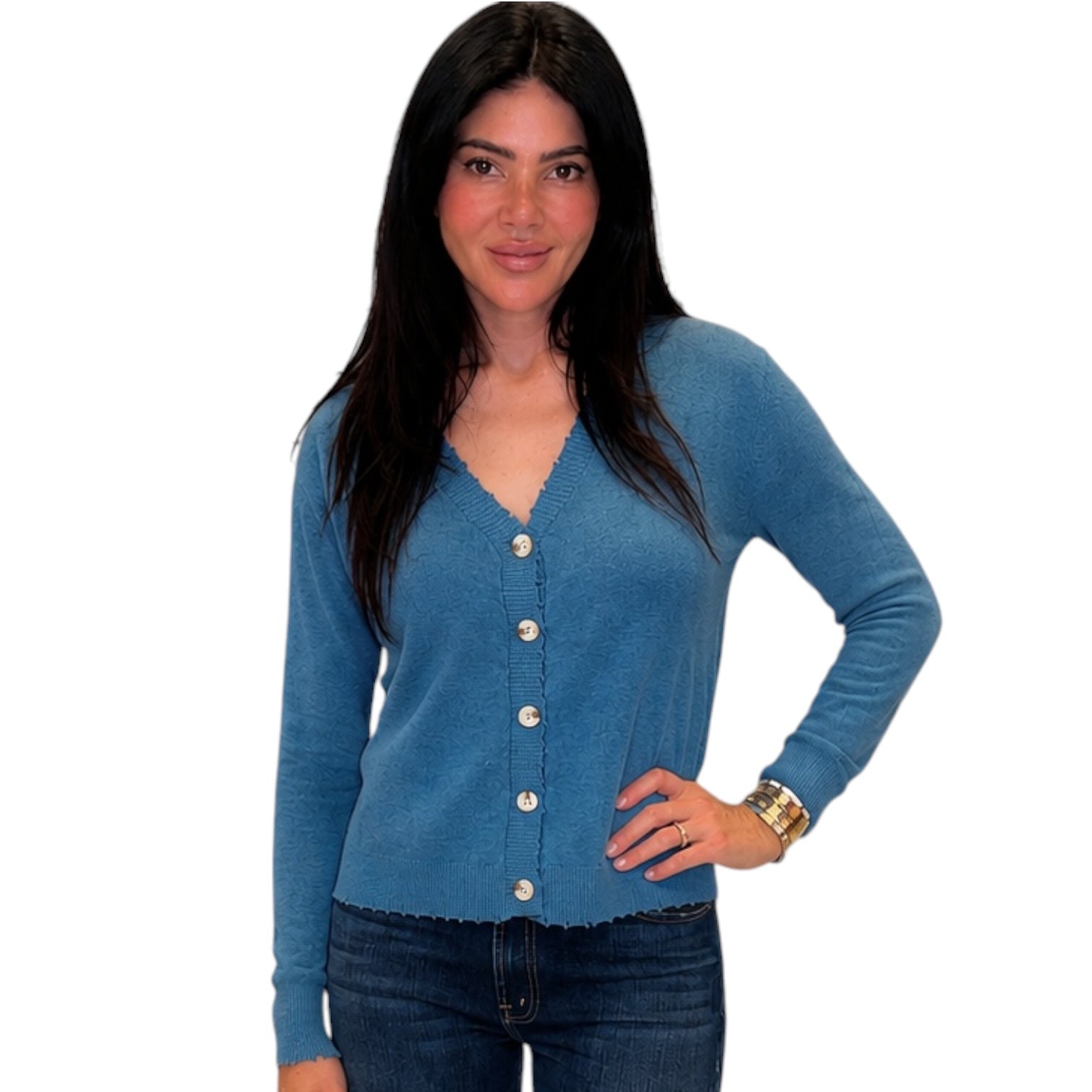 A woman modeling a blue long-sleeve knit cardigan with a scalloped edge and white buttons, paired with dark blue jeans, against a plain white background.