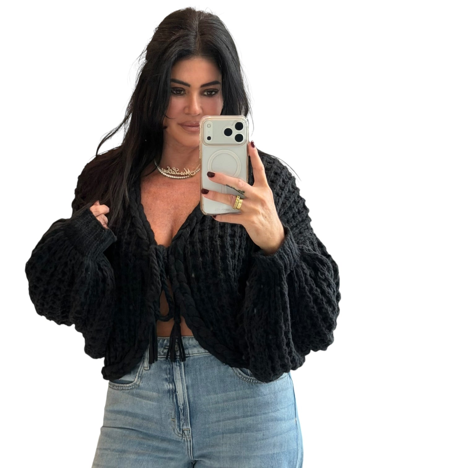 Woman taking a mirror selfie wearing a black knitted cardigan and light blue jeans.