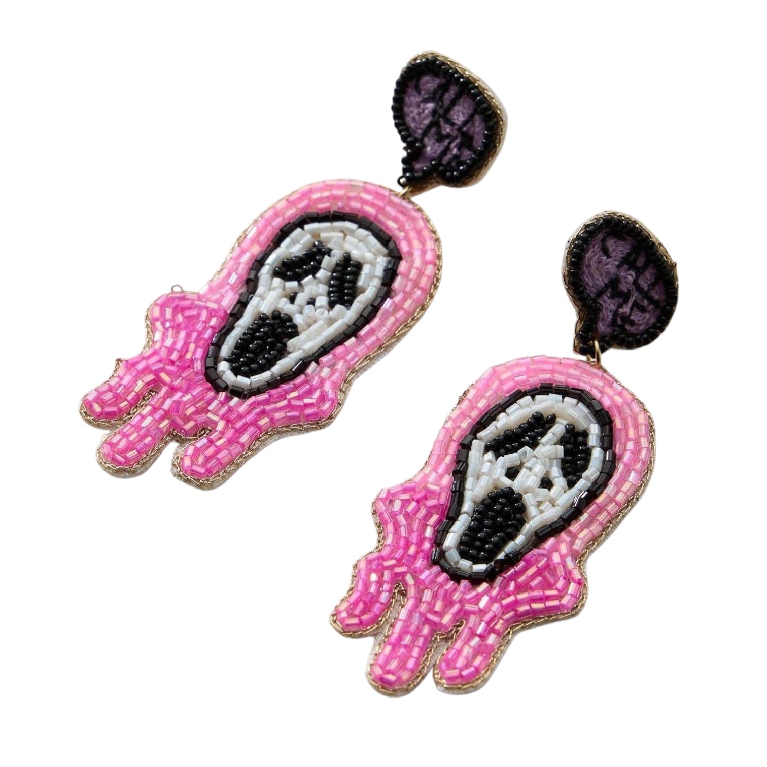 A pair of handmade beaded earrings shaped like stylized pink and white skulls with black details and dark purple backing, shown on a plain white background.