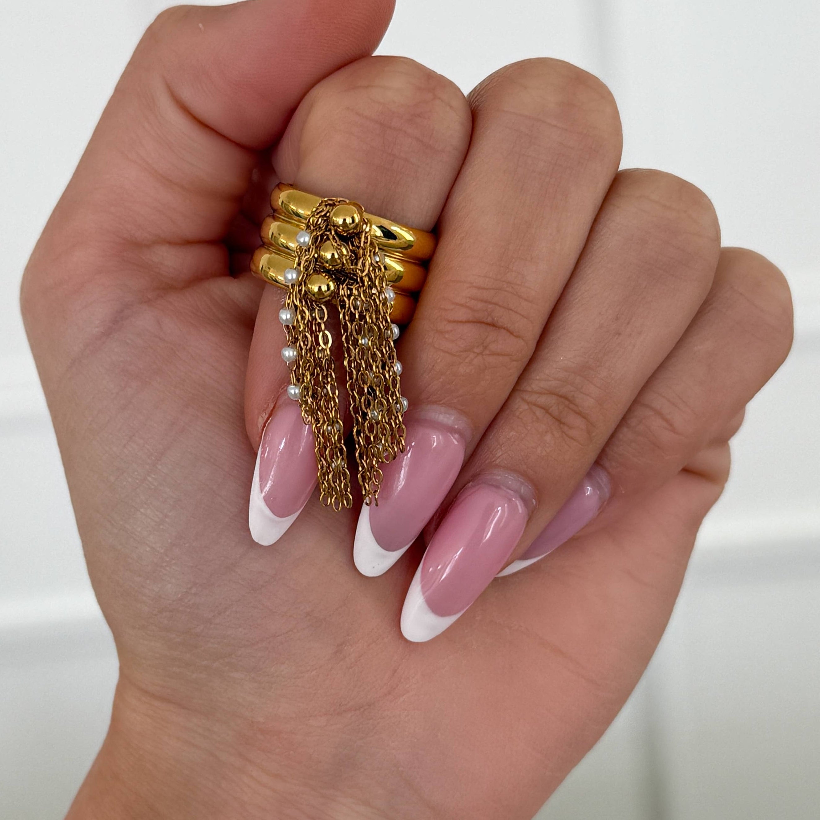 Hand wearing gold ring with chains on a white background