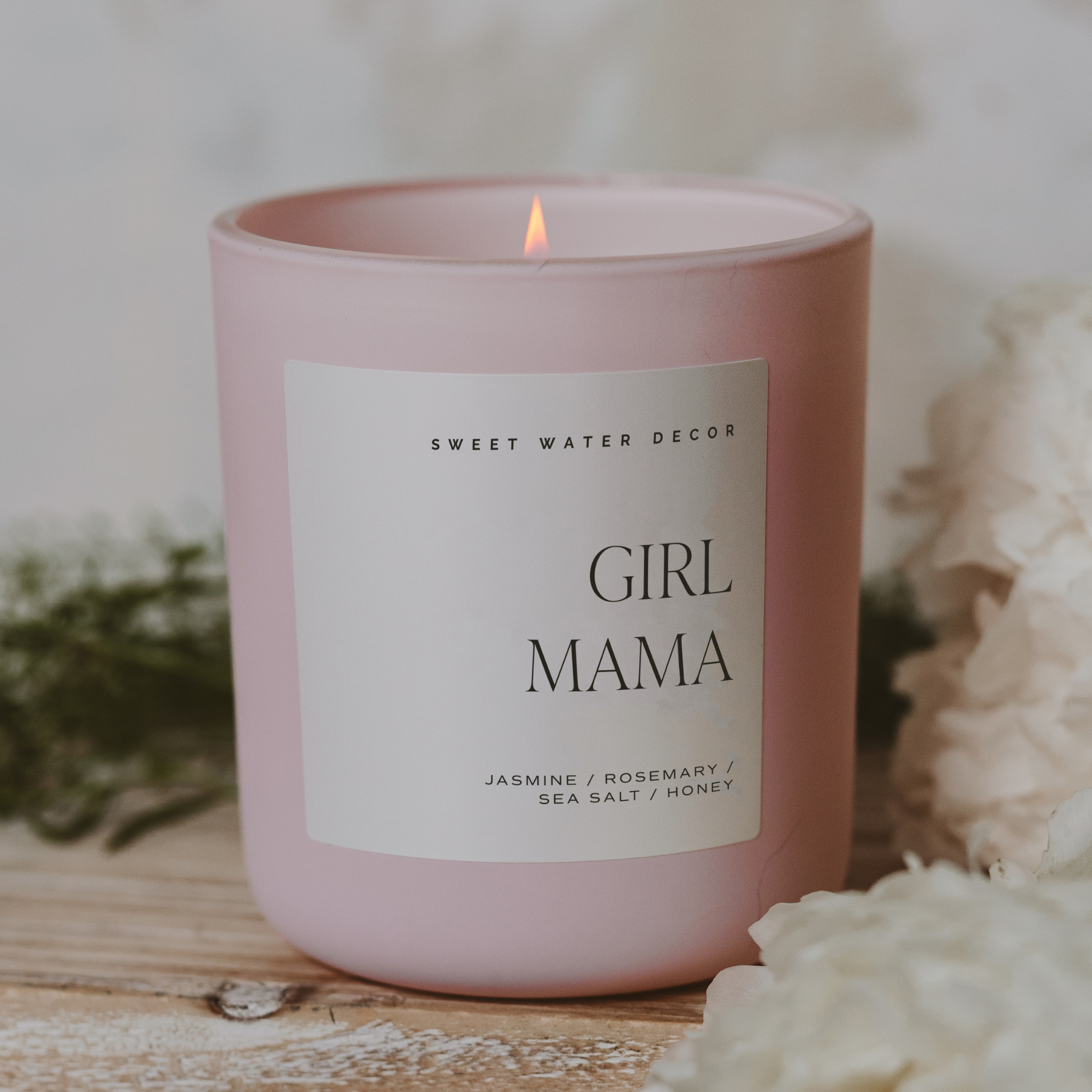 Pink candle labeled 'Girl Mama' by Sweet Water Decor on a wooden surface with decorative elements.