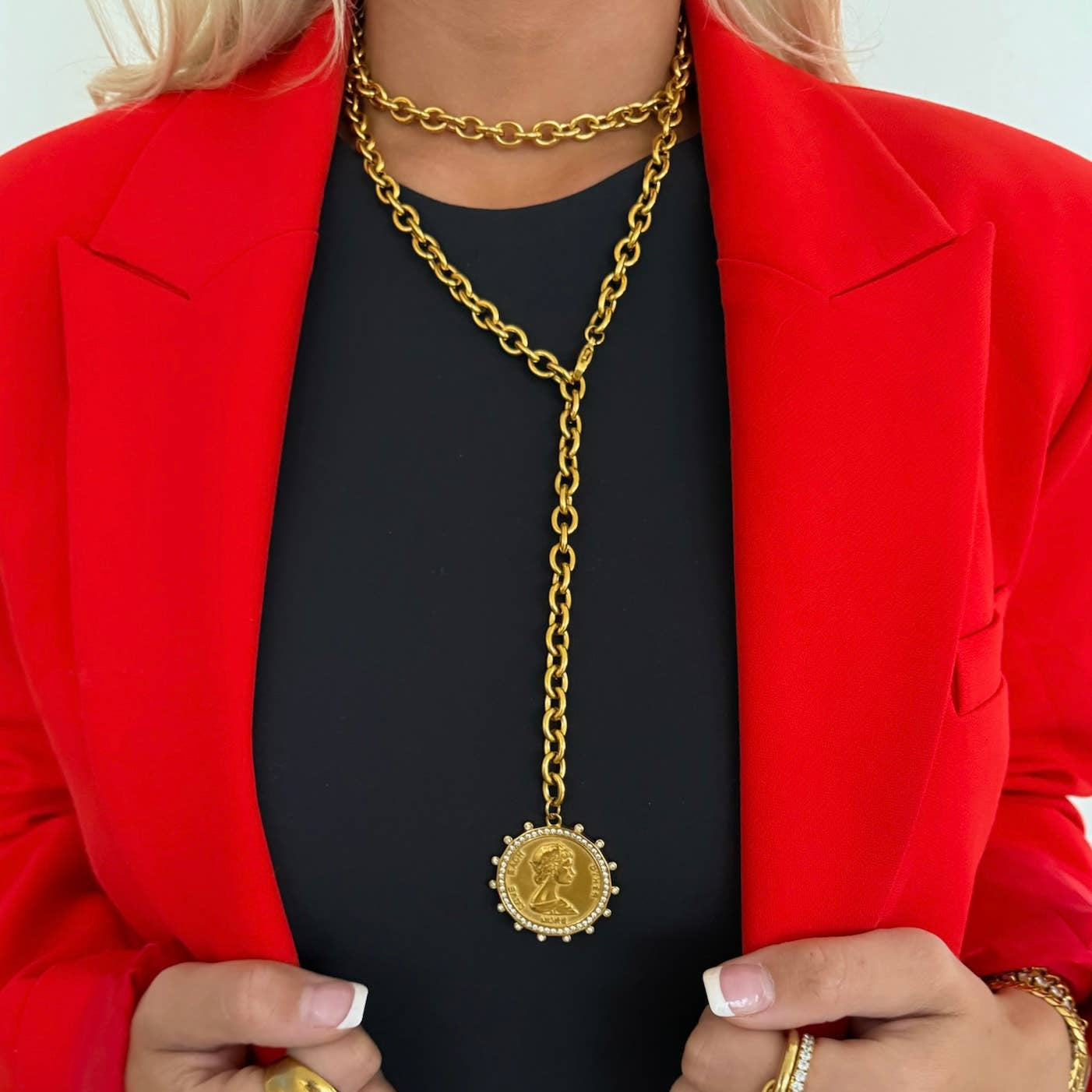 Person wearing a red jacket and black top with a gold chain necklace featuring a coin pendant.