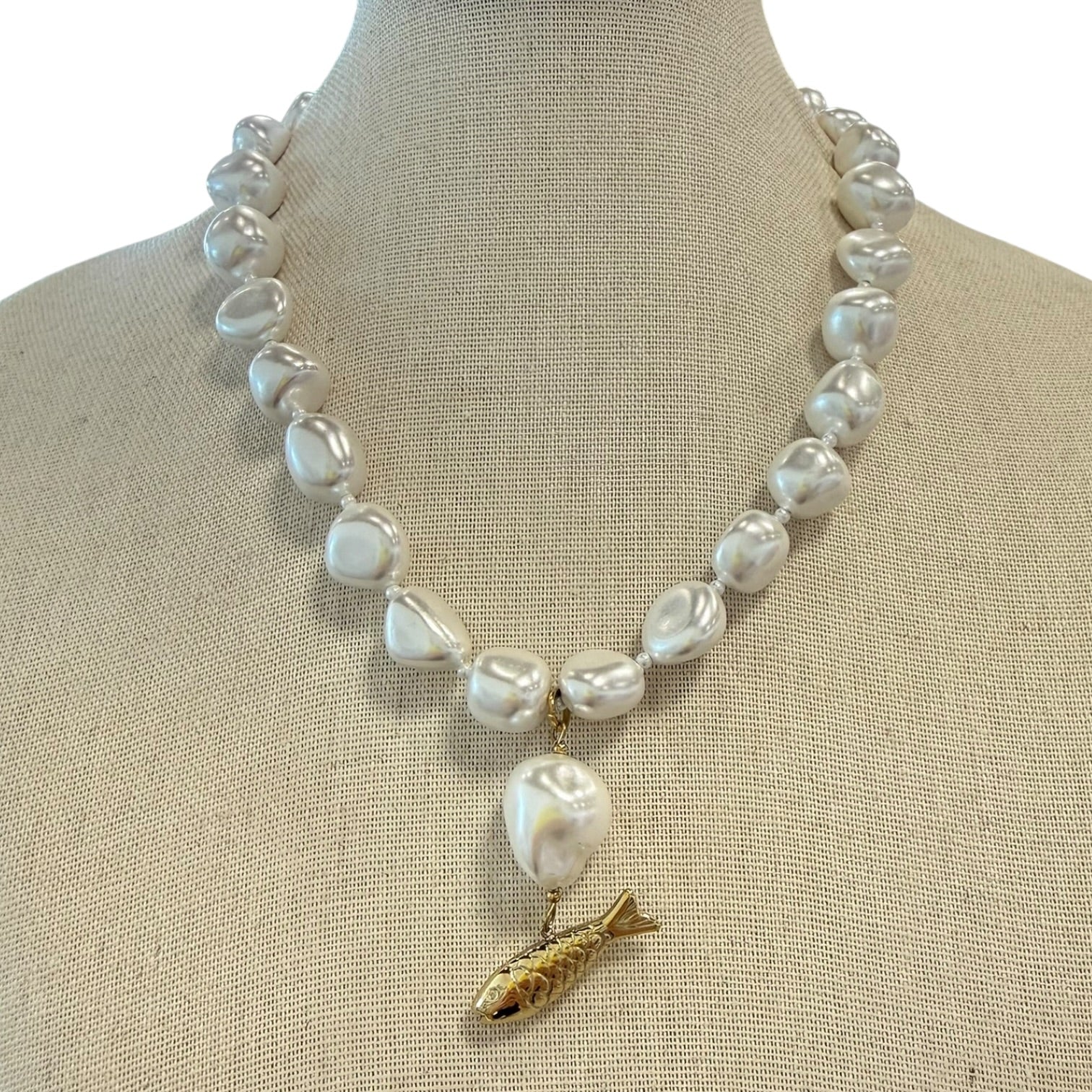 Pearl necklace with a gold fish pendant on a mannequin bust.
