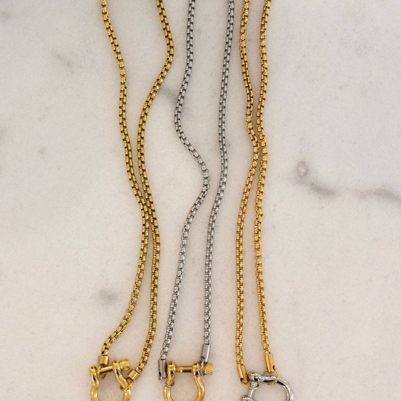 Three gold and silver chain collars on a marble surface
