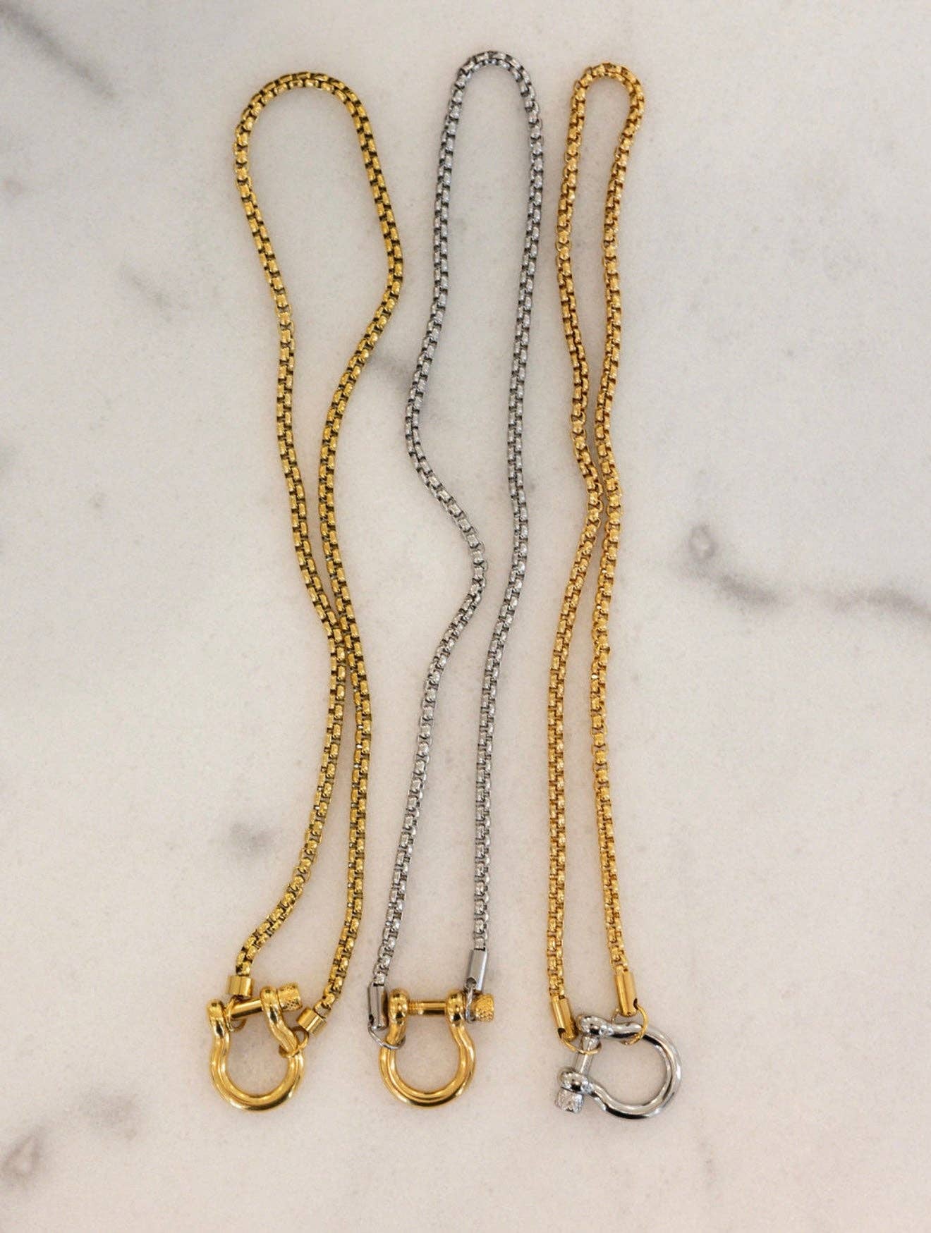 Three gold and silver chain collars on a marble surface