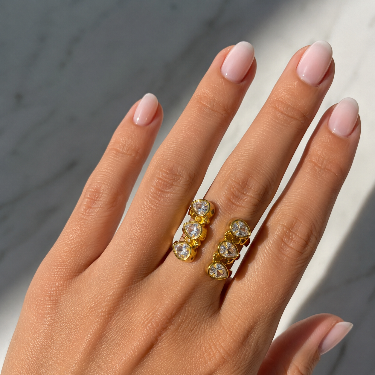 Hand wearing a gold ring with gemstones against a neutral background