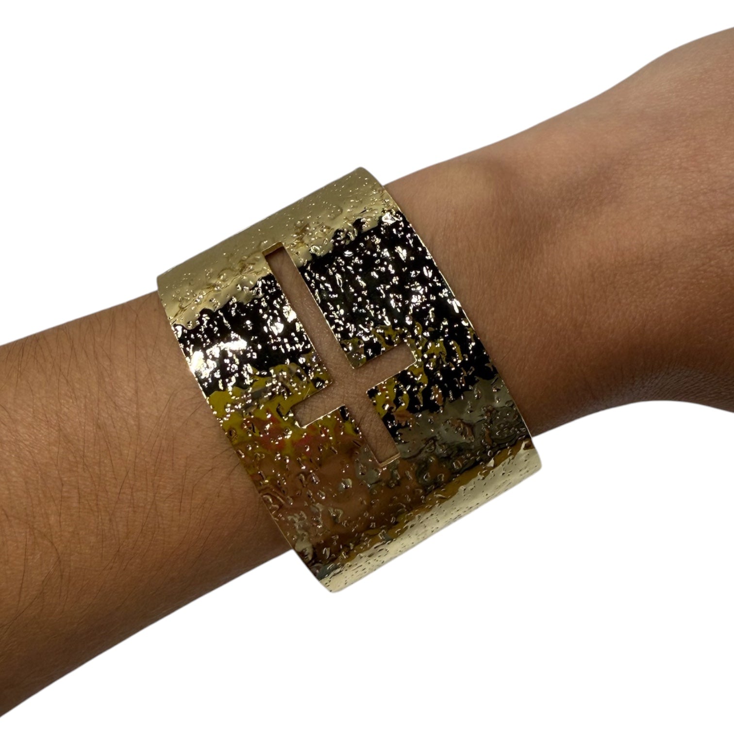 A wide metallic cuff bracelet with a textured gold and black finish, featuring a cutout cross design on the front, shown worn on a person's wrist against a plain white background.