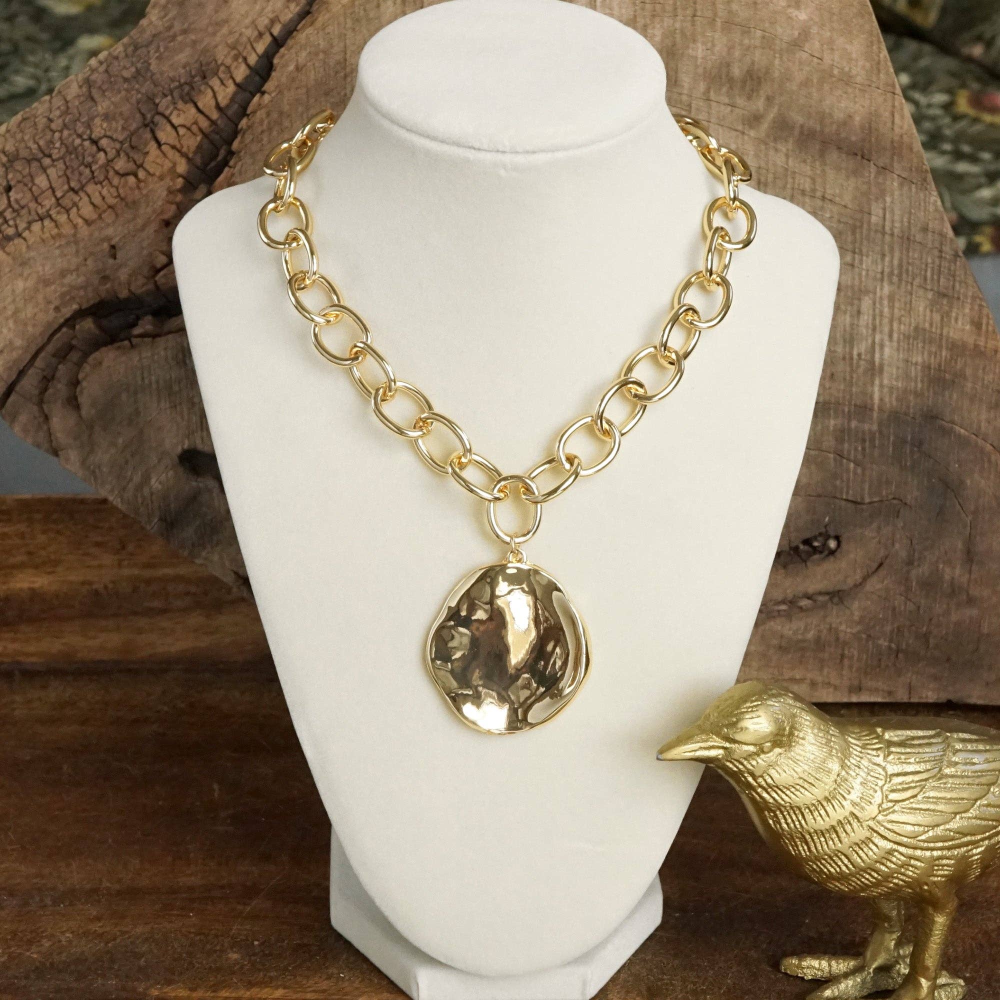 Gold chain necklace with a pendant on a white mannequin bust against a wooden background.
