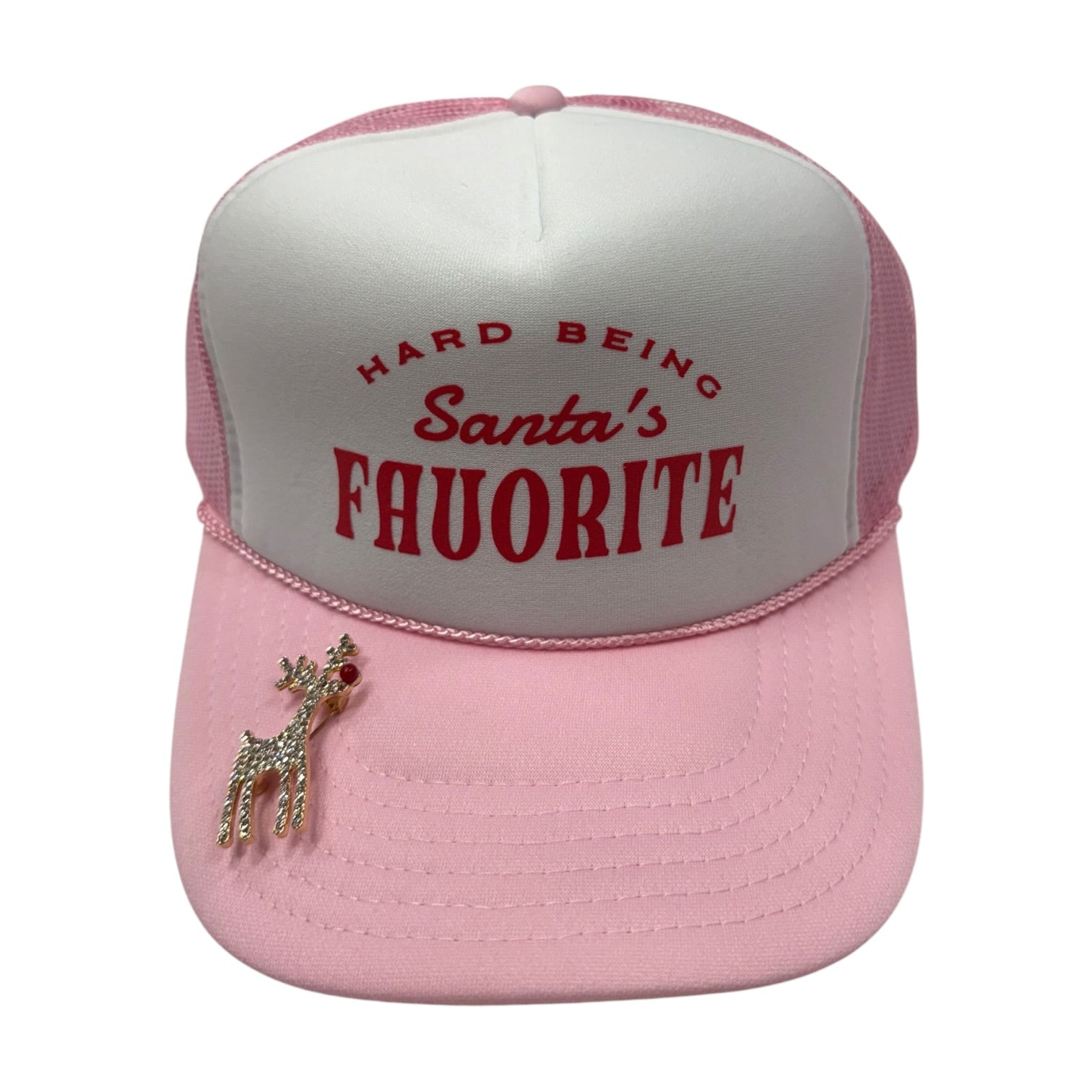 A pink and white trucker hat with red embroidered text reading 'HARD BEING Santa's FAVORITE' on the front panel, plus a small rhinestone reindeer pin on the brim, shown on a plain white background.