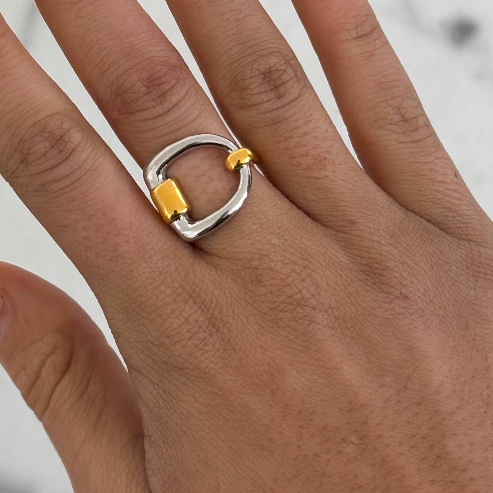 Silver and gold ring on a person's finger with a neutral background