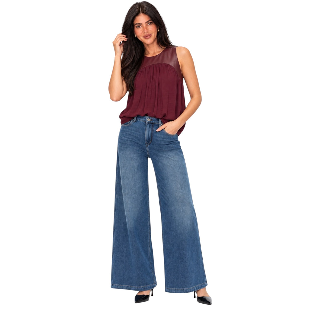 A woman modeling a sleeveless maroon top with sheer shoulder panels and blue wide-leg jeans against a plain white background.