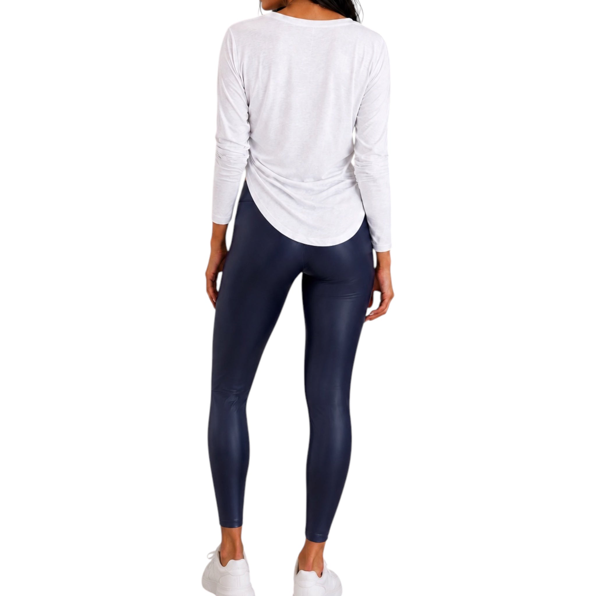 A woman shown from the back wearing a white long-sleeve top and dark navy leggings, standing against a plain white background.