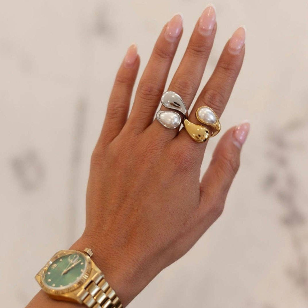 Hand wearing a gold ring with a gold watch on a neutral background