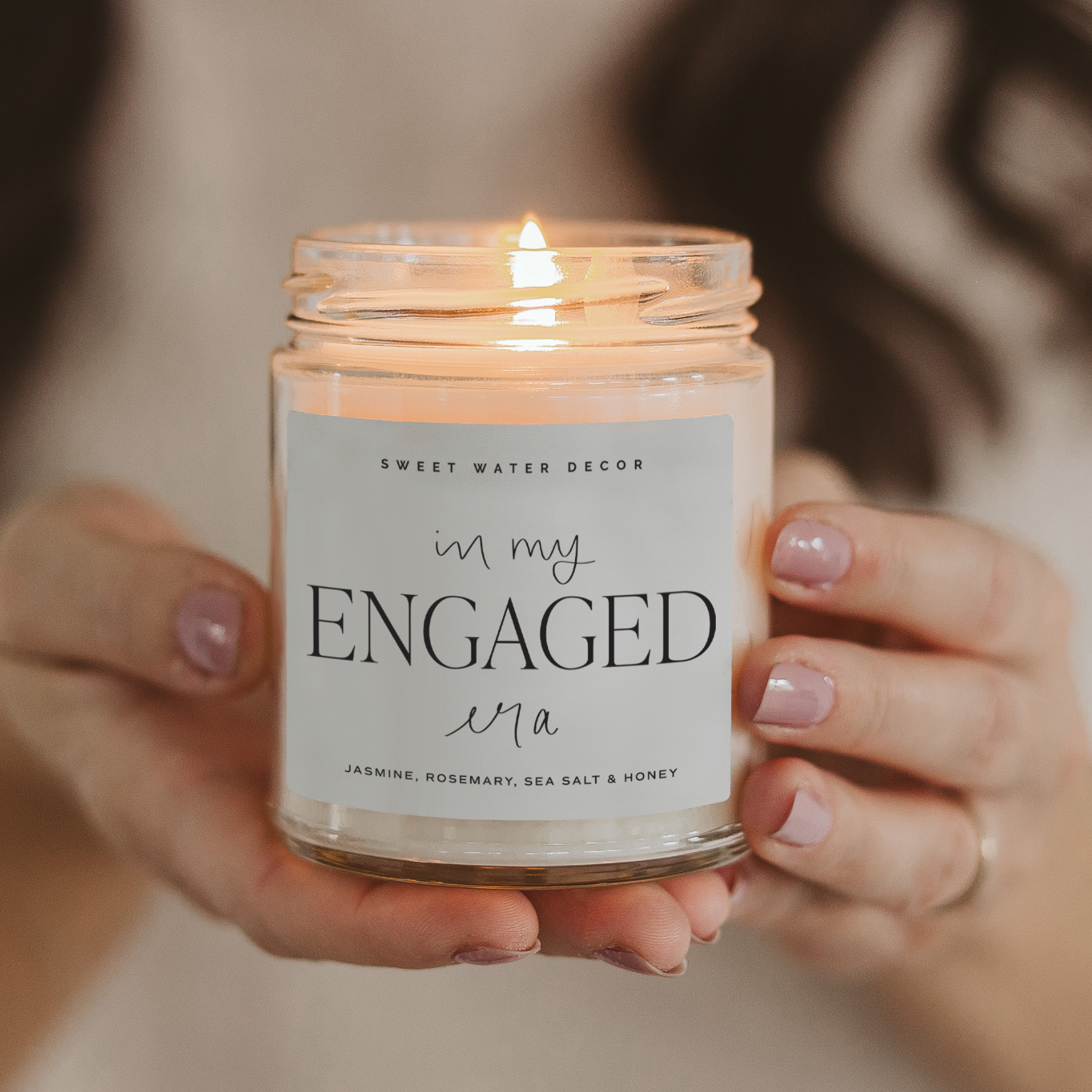 Candle labeled 'in my ENGAGED era' held by a person with a blurred background
