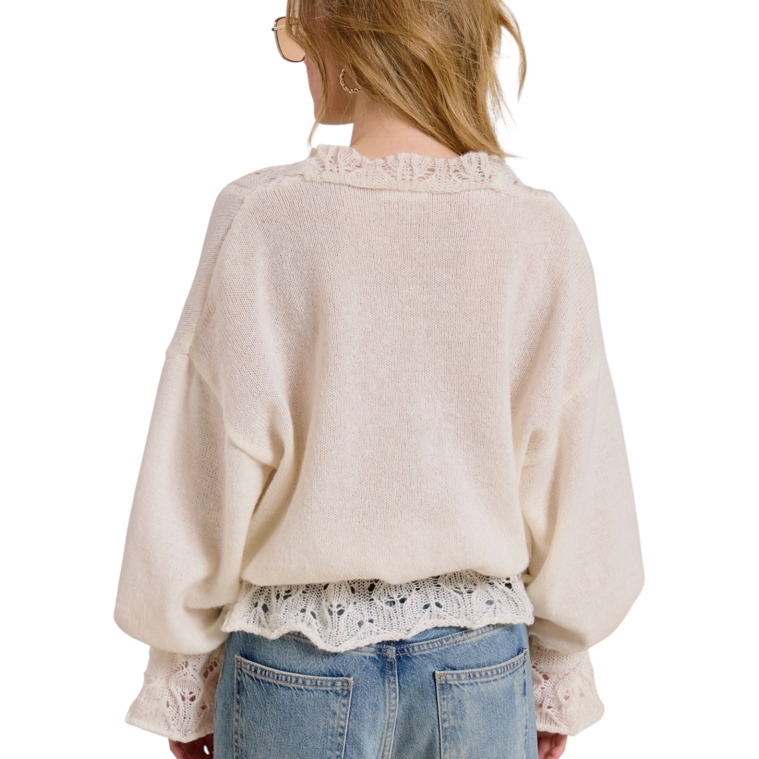 Person wearing a beige sweater with lace details and blue jeans on a white background