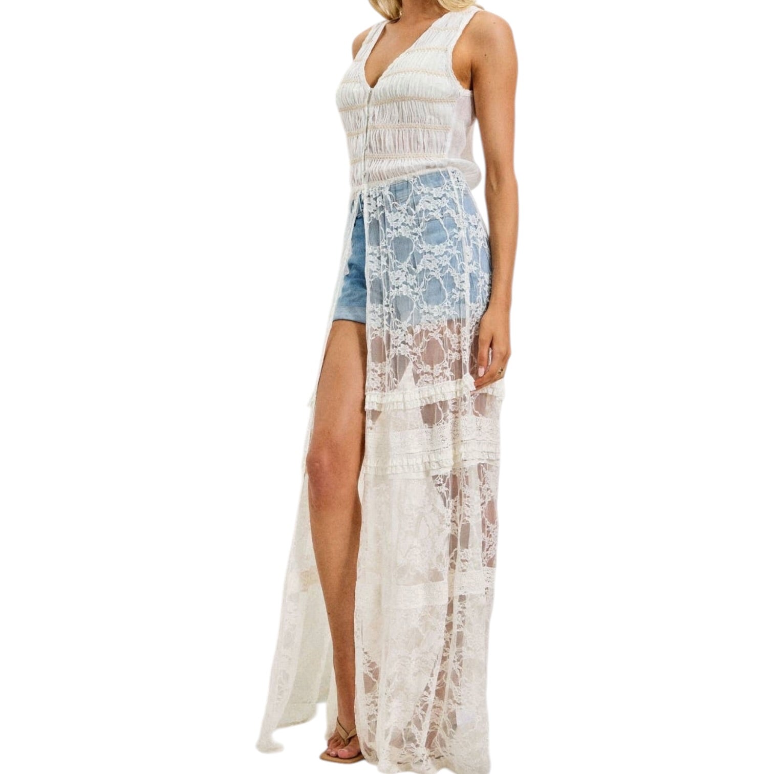 Woman wearing a ivory lace cover-up with denim shorts underneath on a white background
