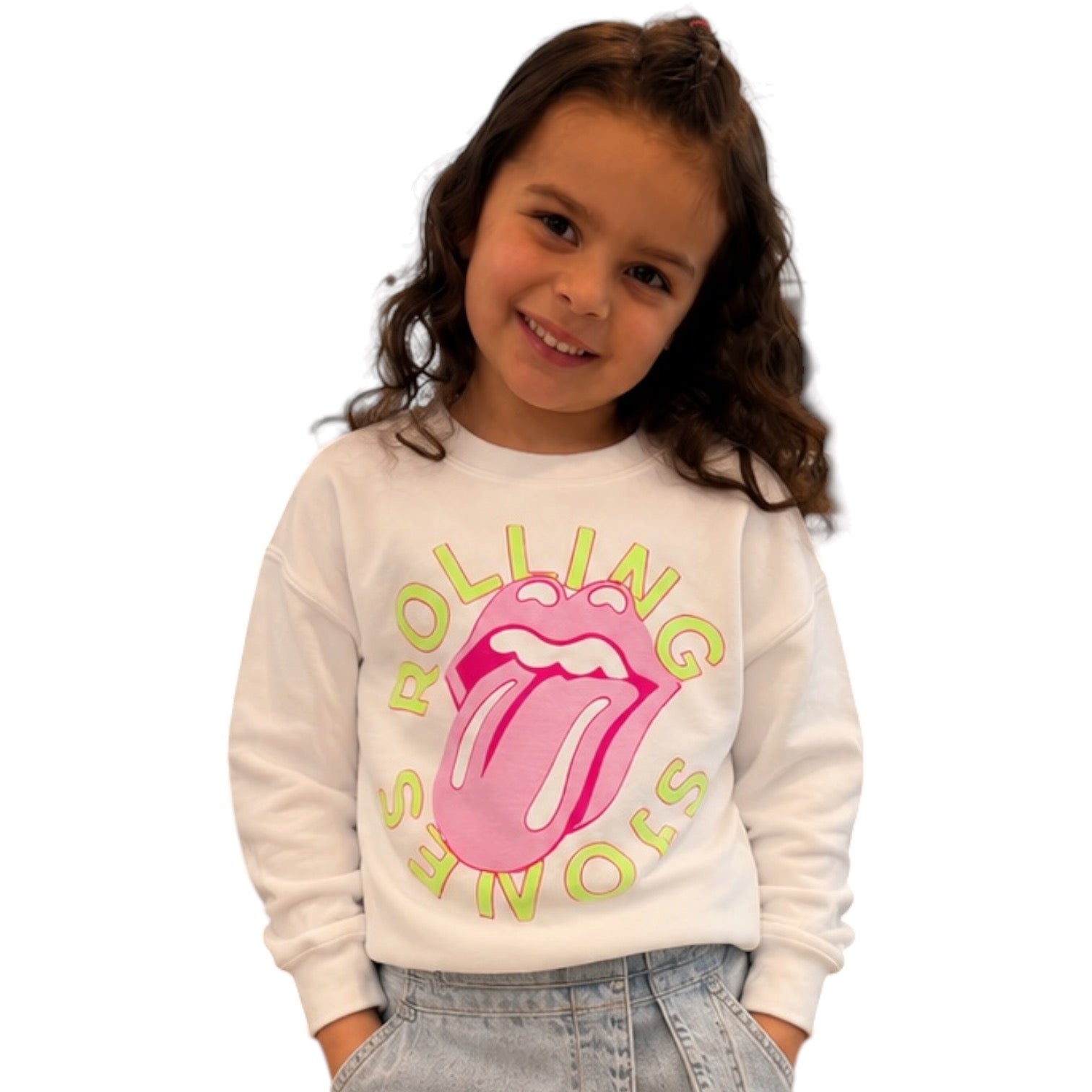 A young girl with brown hair wearing a white crewneck sweatshirt featuring the pink and yellow Rolling Stones tongue logo, paired with light blue jeans, against a plain white background.