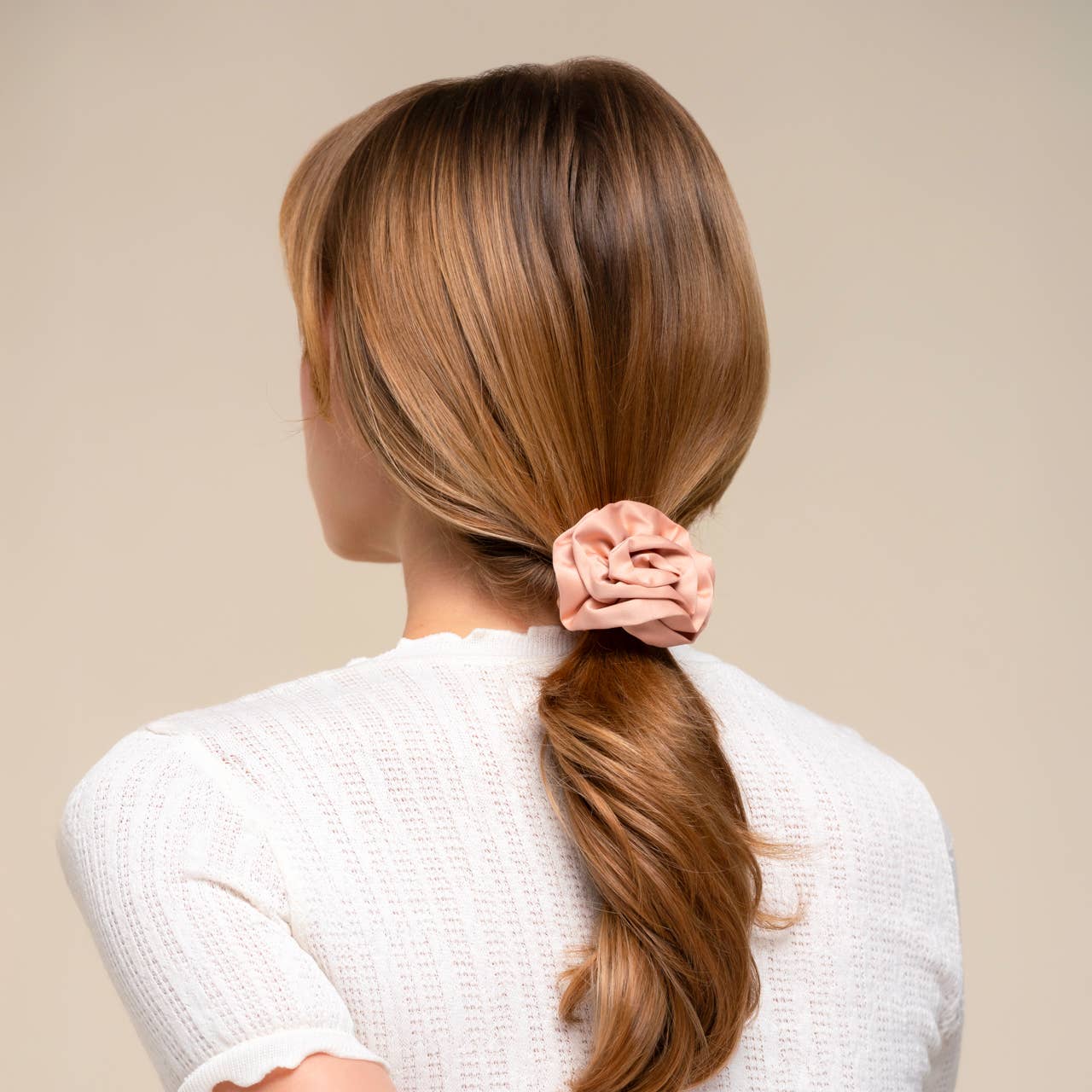 Person with brown hair tied into a ponytail with a pink scrunchie on a beige background