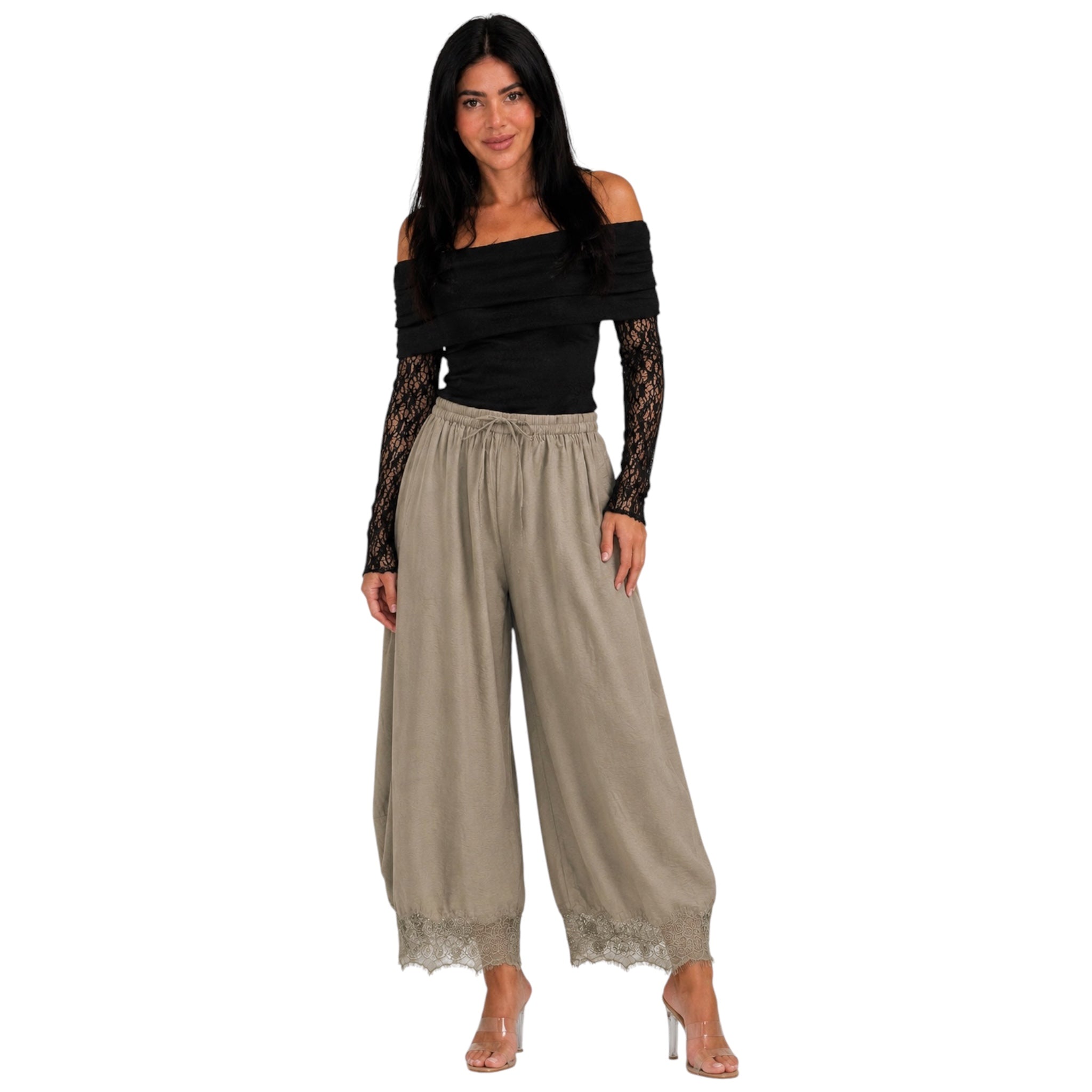 A woman modeling a pair of wide-leg beige pants with lace trim and a black off-the-shoulder top with black lace sleeves, set against a plain white background.