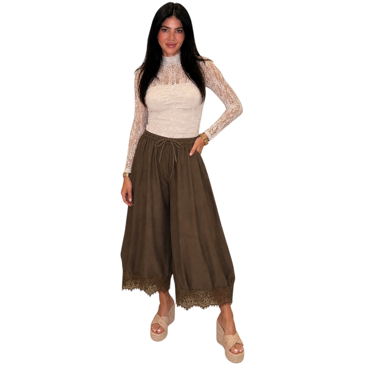 A woman modeling a two-piece outfit consisting of a cream lace long-sleeve top and brown wide-leg pants with lace trim, set against a plain white background.