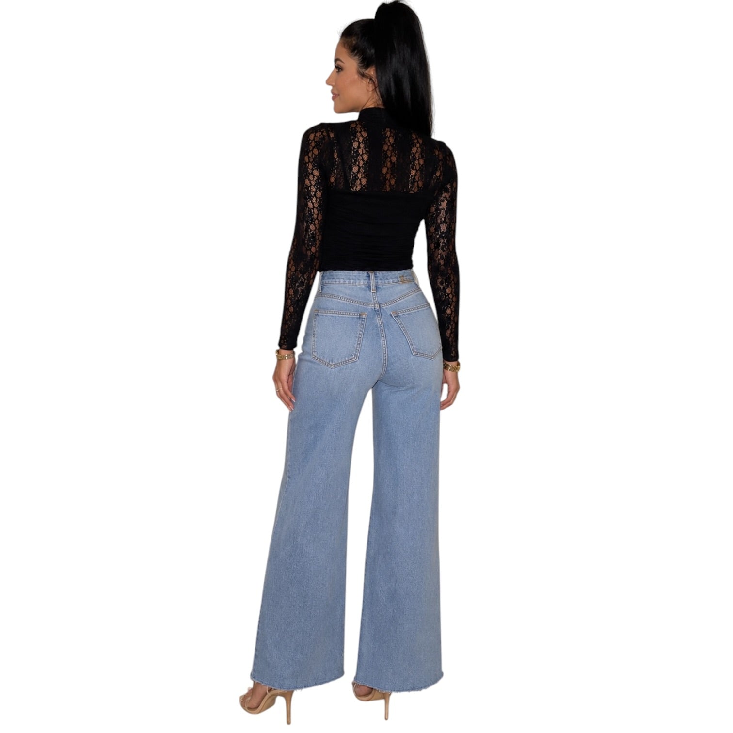A woman shown from the back wearing a black long-sleeve lace top and light blue wide-leg jeans, standing against a plain white background.