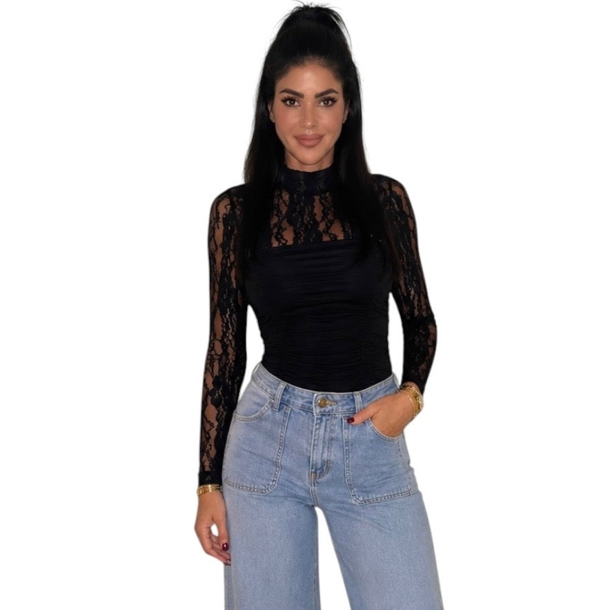 A woman modeling a black long-sleeve mock neck top with sheer black lace sleeves, paired with light blue jeans, against a plain white background.