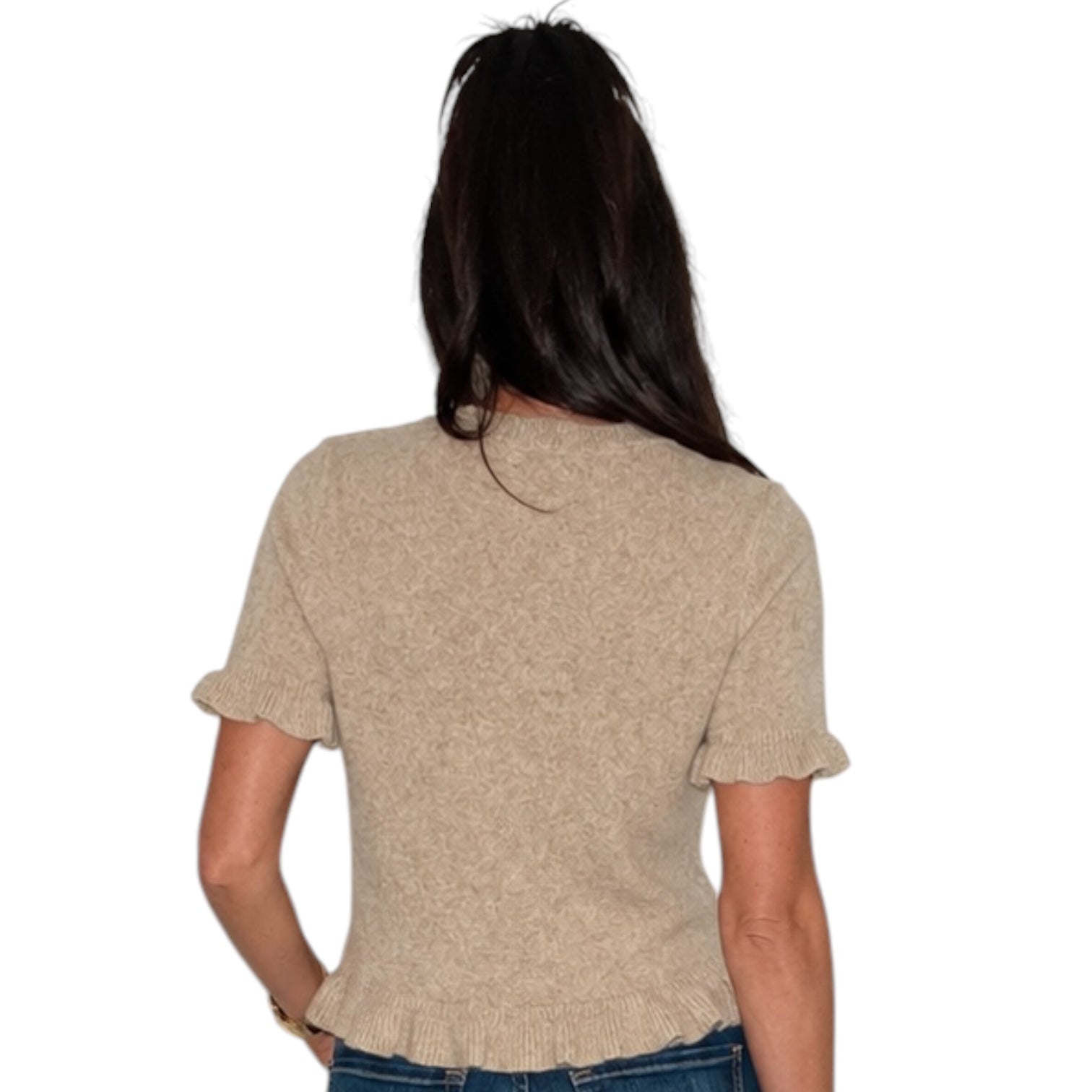 A woman viewed from the back wearing a short-sleeve knit top in a light beige or oatmeal color, paired with blue jeans, against a plain white background.
