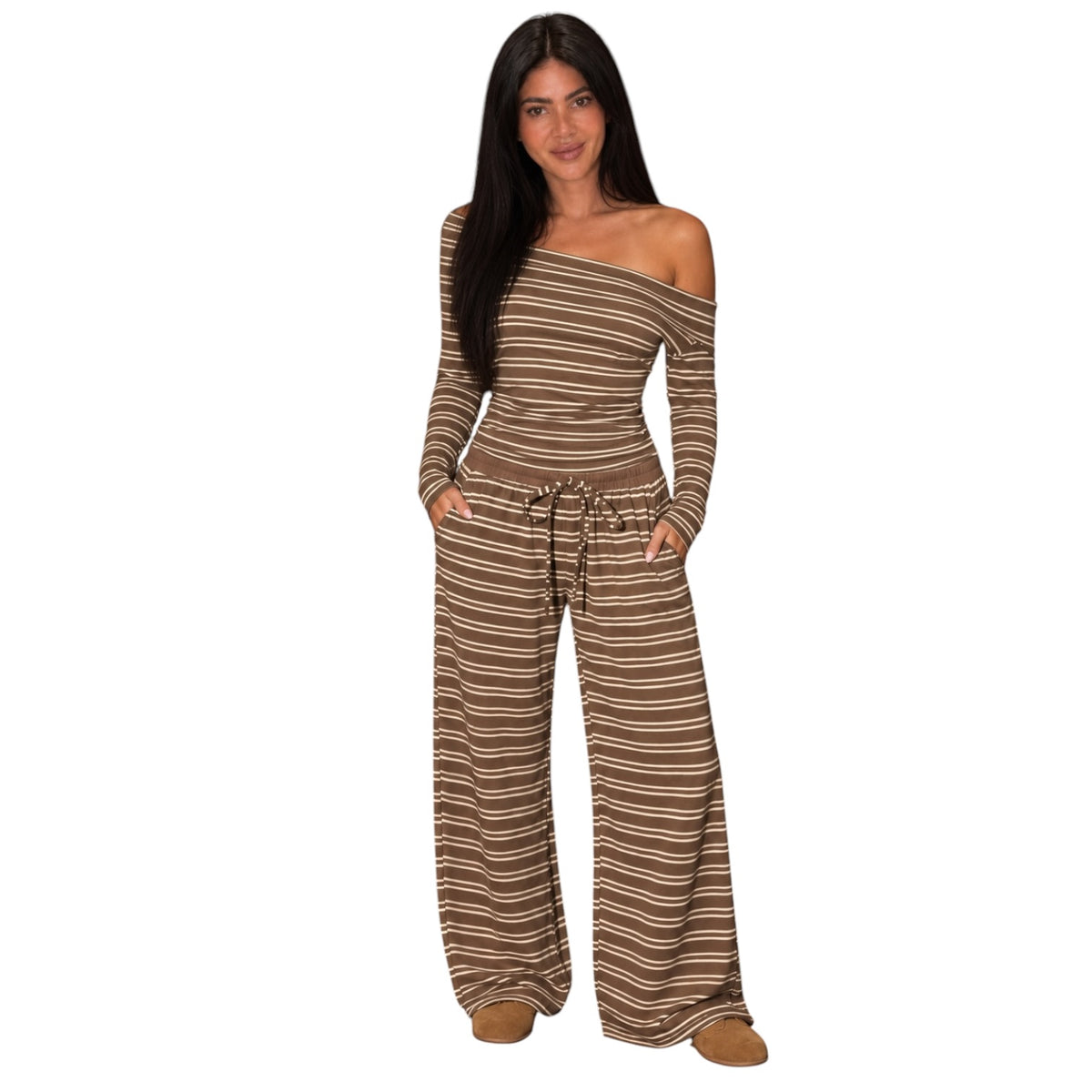 A woman modeling a brown and beige striped off-the-shoulder jumpsuit with wide legs and a drawstring waist, set against a plain white background.