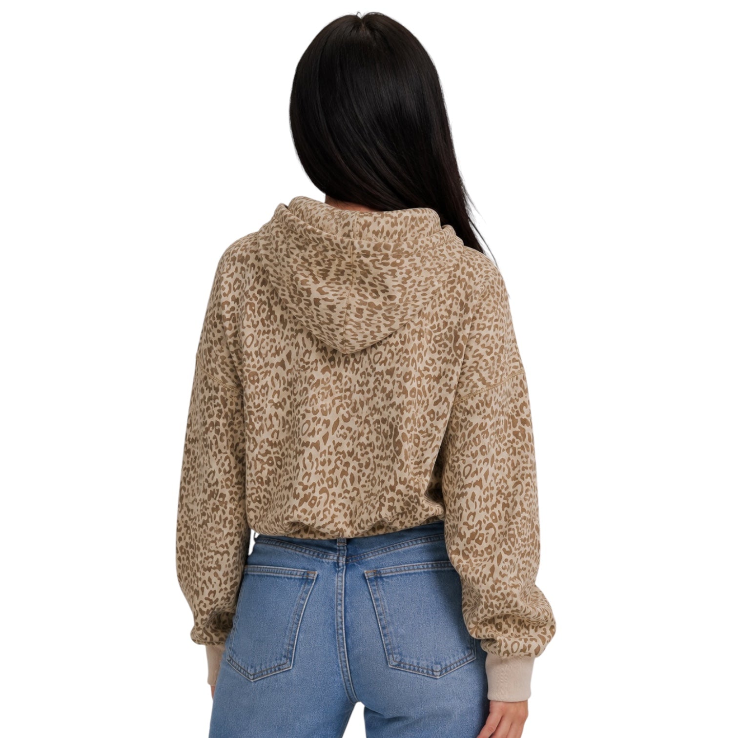 A woman viewed from the back wearing a beige and brown leopard-print cropped hoodie with light beige ribbed cuffs, paired with blue jeans, against a plain white background.