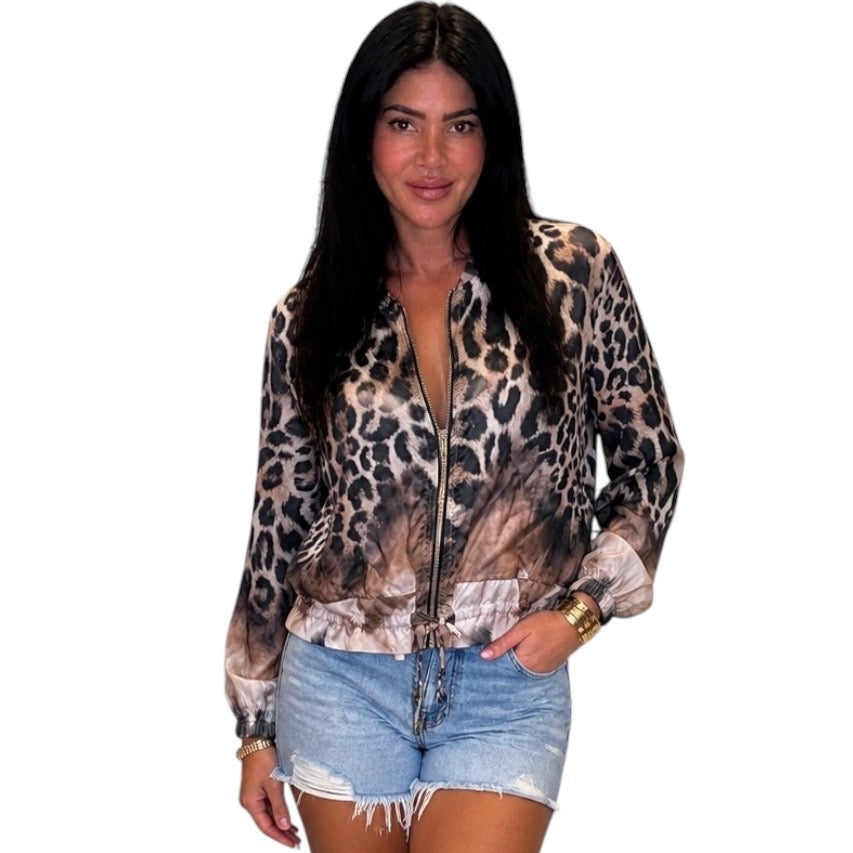 A woman modeling a leopard print zip-up jacket with sheer sleeves and denim shorts against a plain white background.