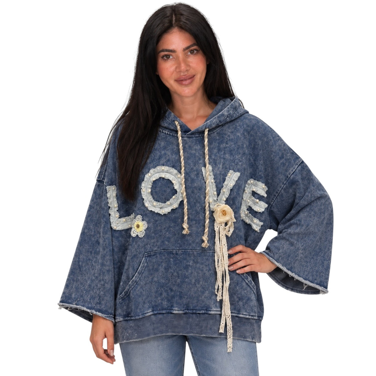 A woman modeling a blue acid-wash hoodie with 'LOVE' spelled out in white textured letters across the chest, decorated with macrame and beads, set against a plain white background.