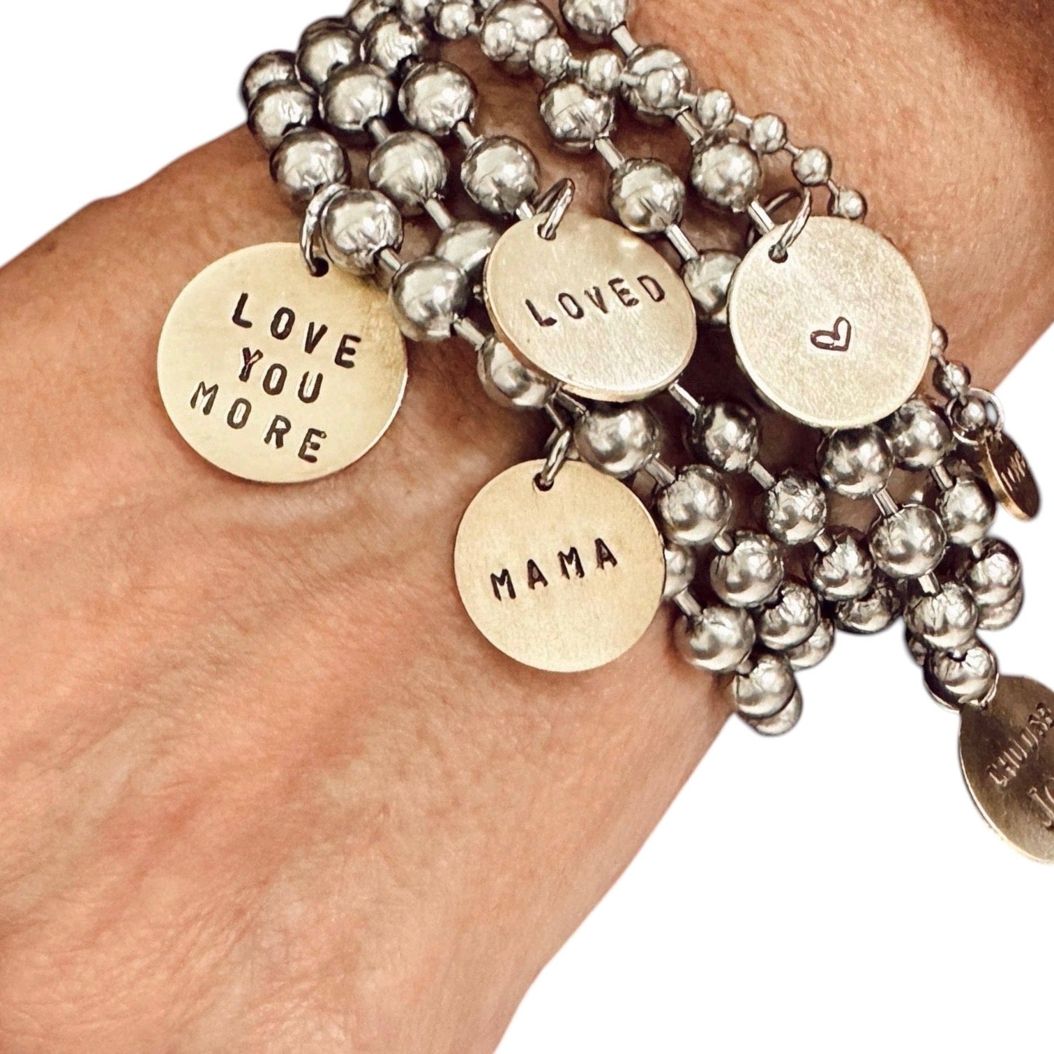 Stack of silver beaded bracelets with gold charm tags on a wrist.