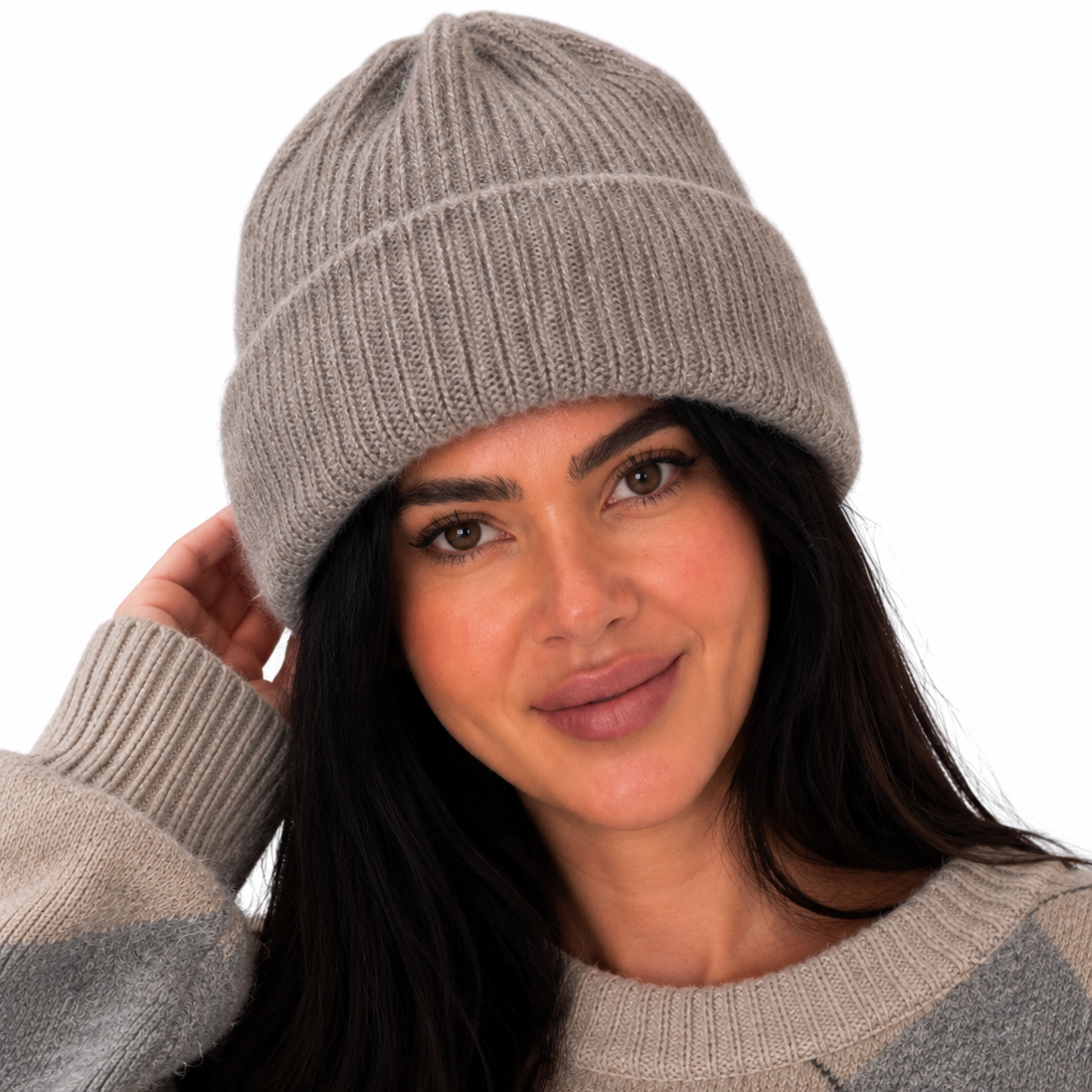 A woman wearing a light gray ribbed knit beanie and a beige and gray argyle sweater, posing against a solid white background.