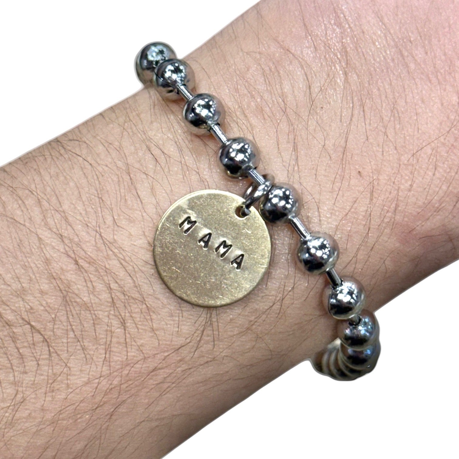 Bracelet with 'MAMA' charm on a wrist against a white background