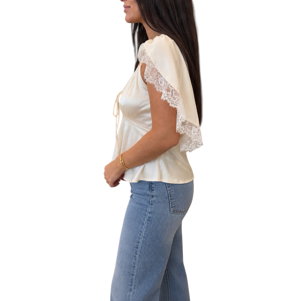 A woman shown in side profile wearing a cream satin blouse with lace flutter sleeves and light blue jeans, against a plain white background.