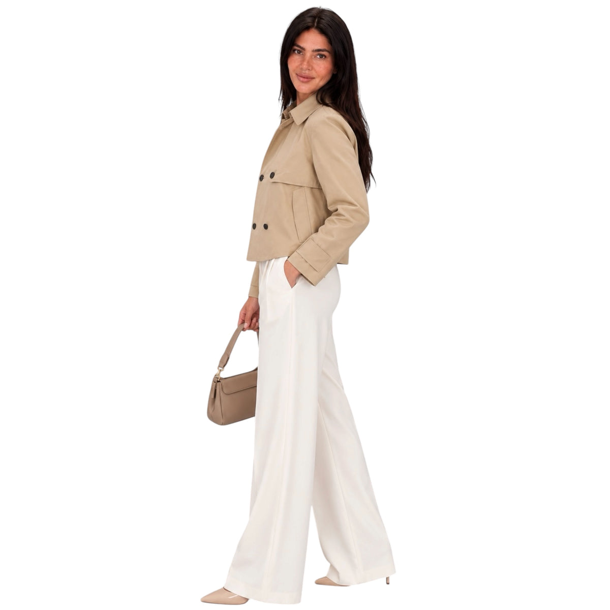 A woman modeling a cropped beige double-breasted jacket with white wide-leg trousers, holding a beige handbag against a solid white background.