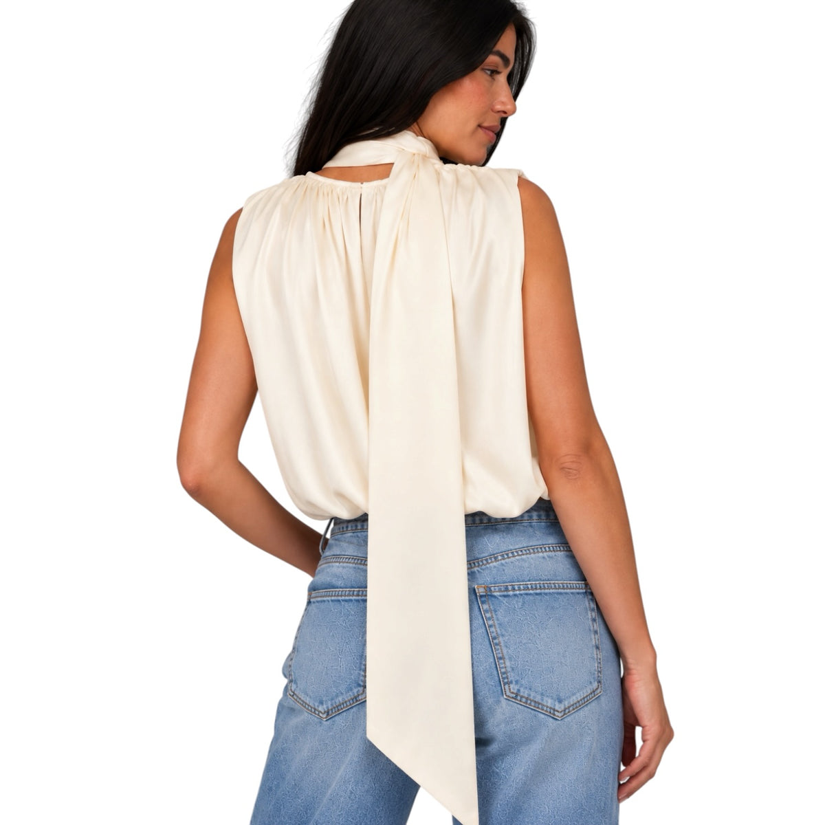 A woman shown from the back wearing a sleeveless cream-colored blouse with a long draped tie detail at the back, paired with light blue jeans, against a plain white background.