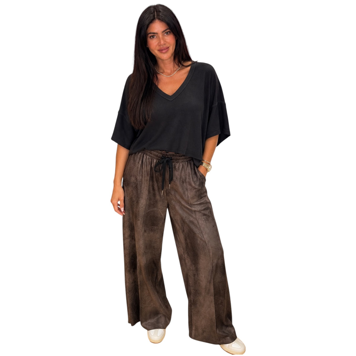 A woman modeling a black short-sleeve V-neck top and brown wide-leg tie-waist pants against a plain white background.