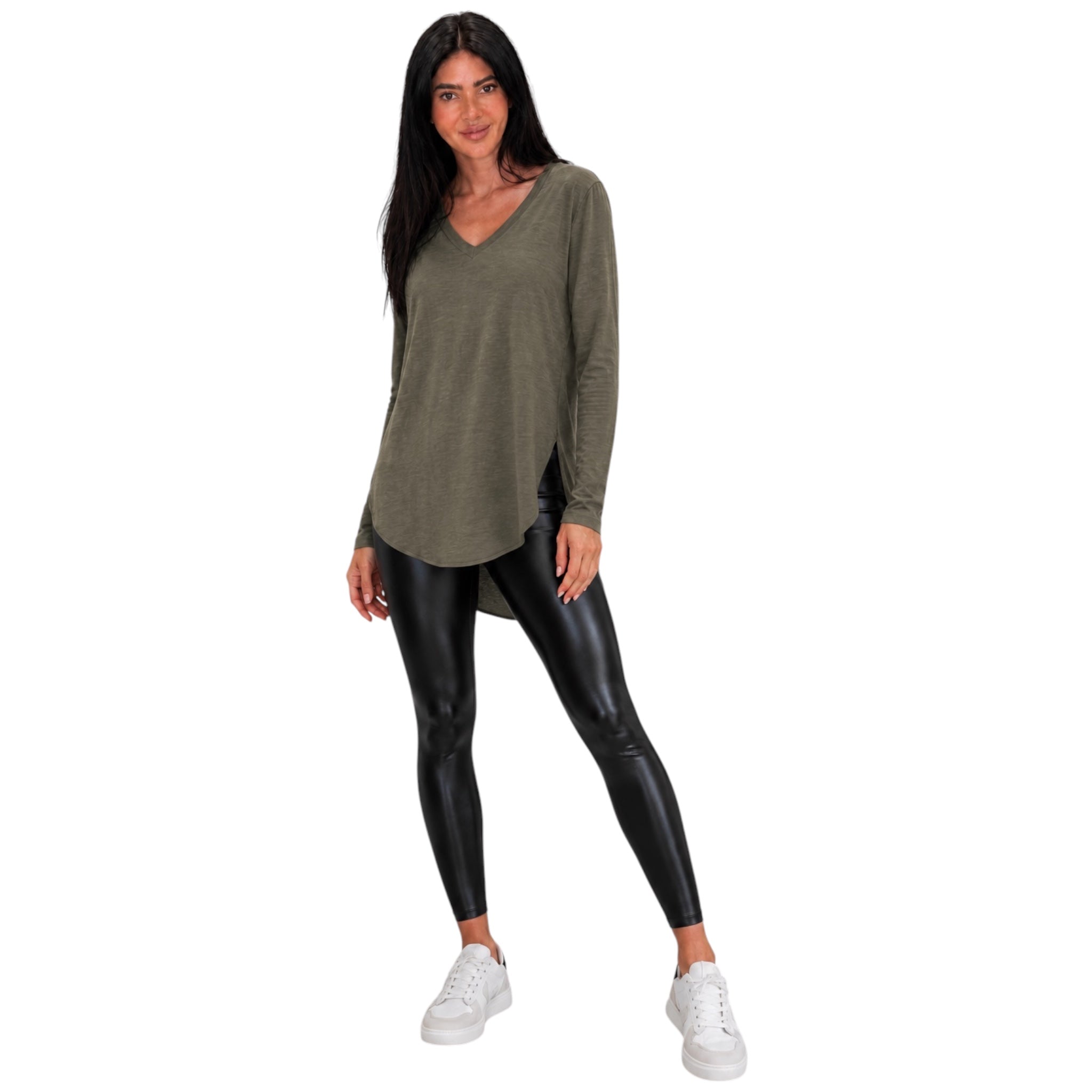A woman modeling a long-sleeve olive green V-neck top with black faux-leather leggings and white sneakers, set against a plain white background.
